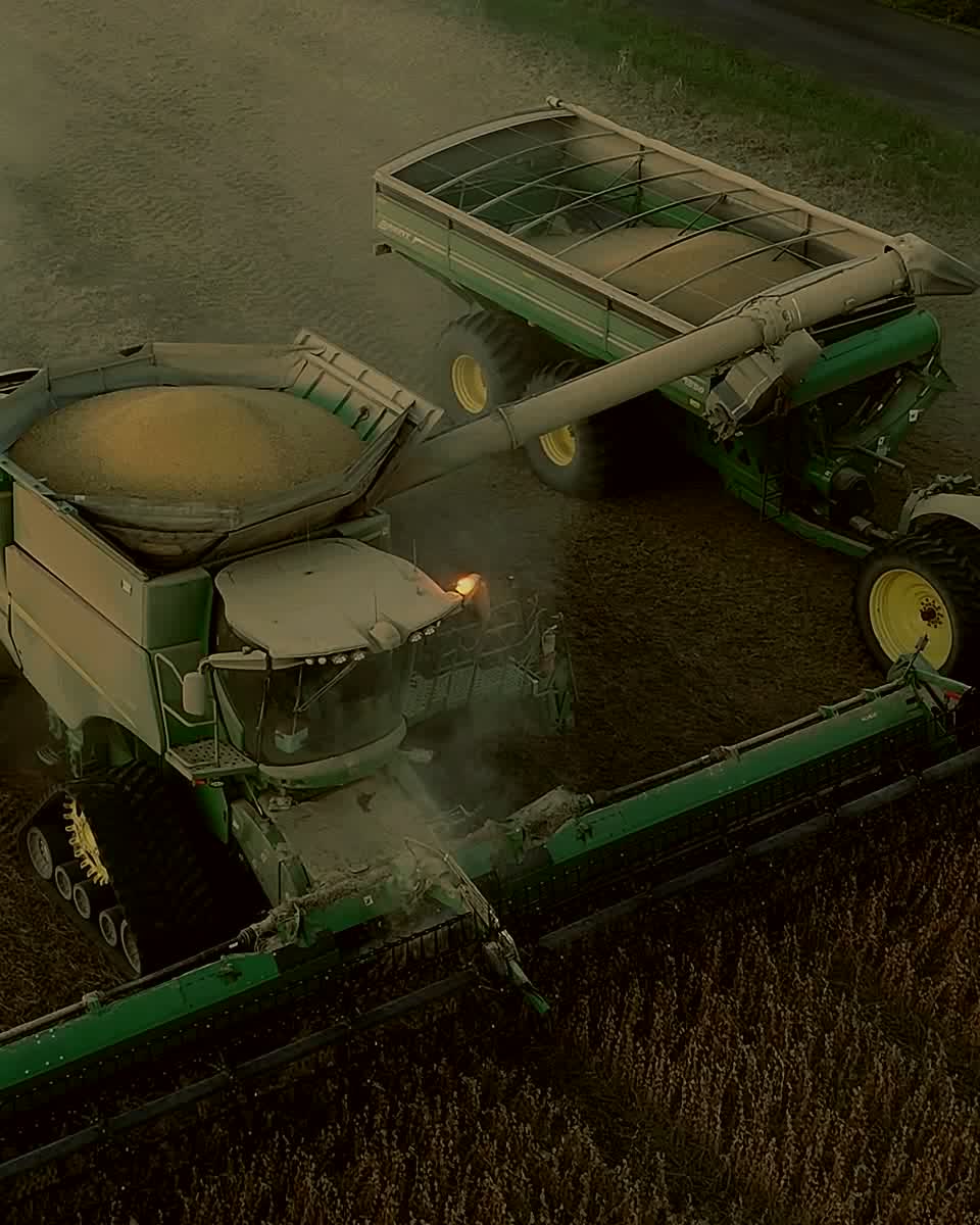 A combine unloading soybeans into a grain cart at dusk